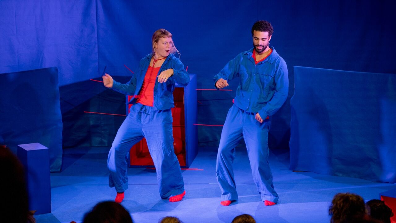 Julius Schraven en Meghan Dobbelsteijn-Bisschops dansen in blauw en rode kleding met blauw en rood decor op de achtergrond