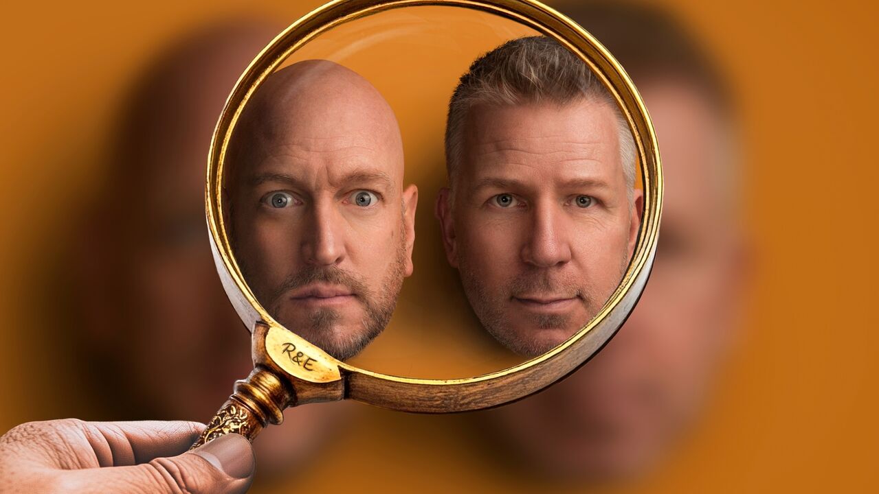 Een hand houdt een vergrootglas vast. Door het vergrootglas zijn de gezichten van Rob en Emiel zichtbaar